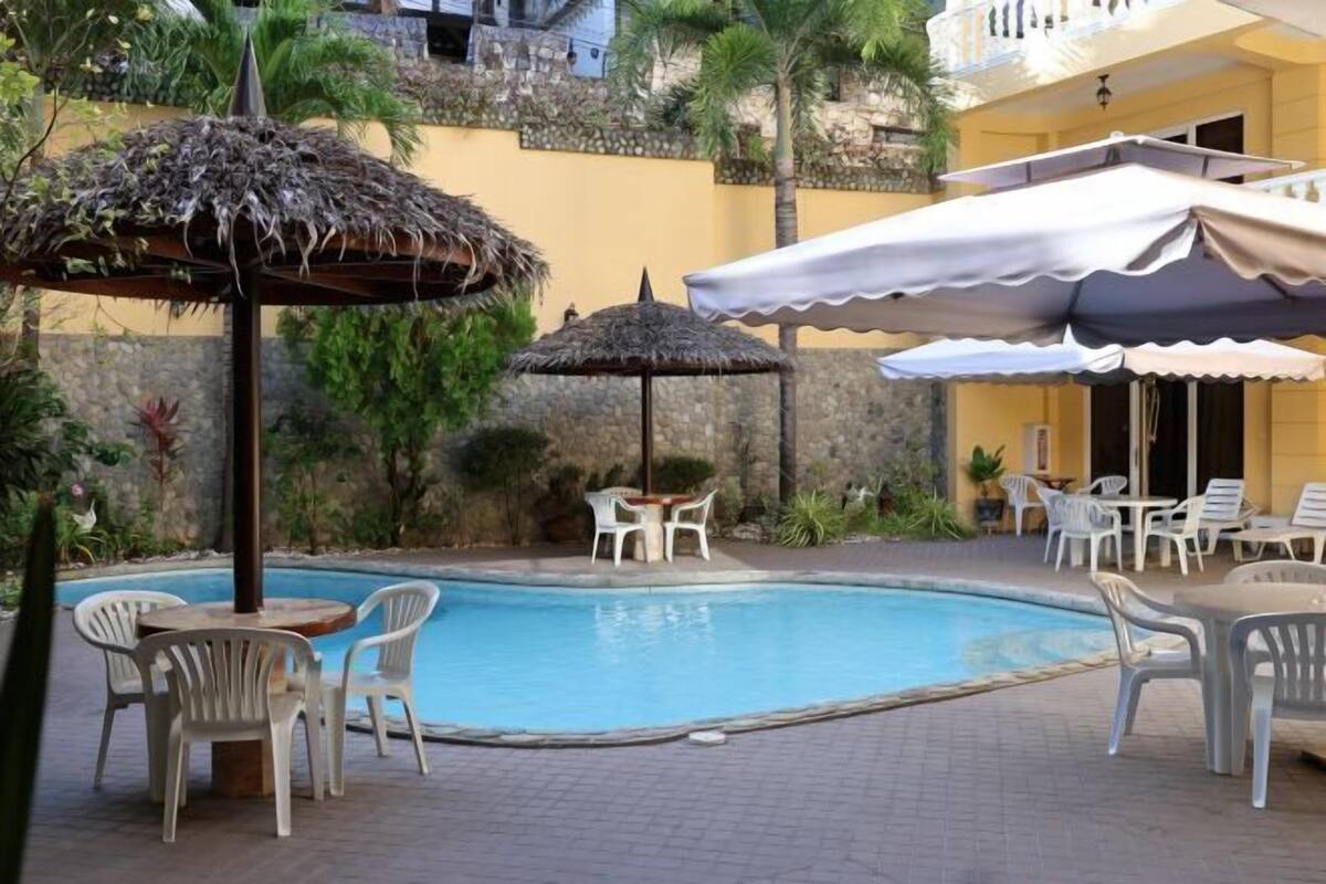 A pool area with chairs and umbrellas, surrounded by plants and a building.