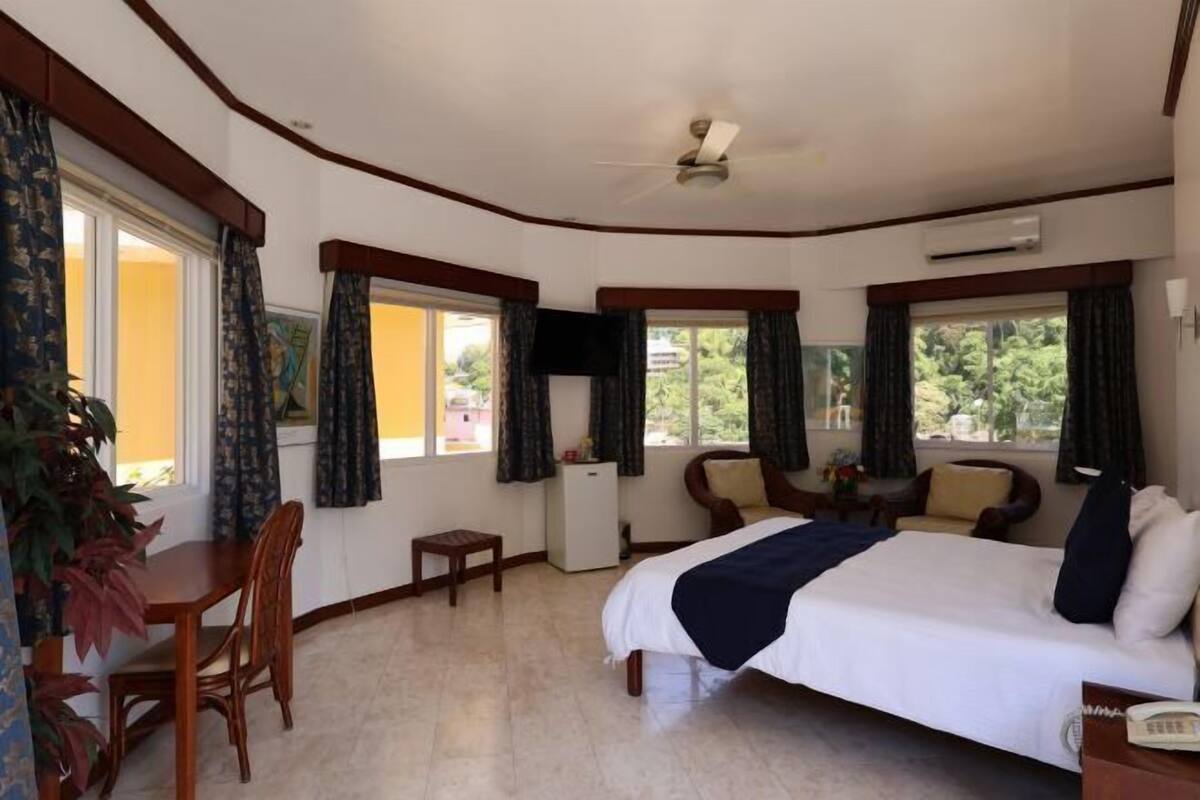 A bedroom with a bed, a desk, a chair, a small table, and a ceiling fan.