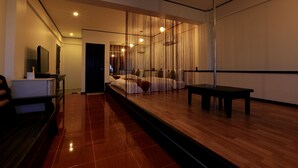 A modern hotel room with a wooden floor, a bed with white bedding, a small table, and a TV on a stand. - Mermaid Resort and Dive Center (Puerto Galera)