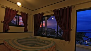 A spa room with a stone hot tub, large windows with curtains, and a view of the sunset. - Mermaid Resort and Dive Center (Puerto Galera)