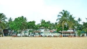 Een hotel aan het strand met meerdere kamers, terras en palmbomen.