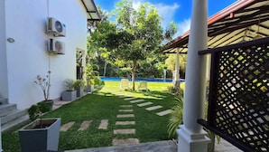 A courtyard with a swimming pool, a lawn, and a pergola structure. - Riverside Cabanas (Mirissa)