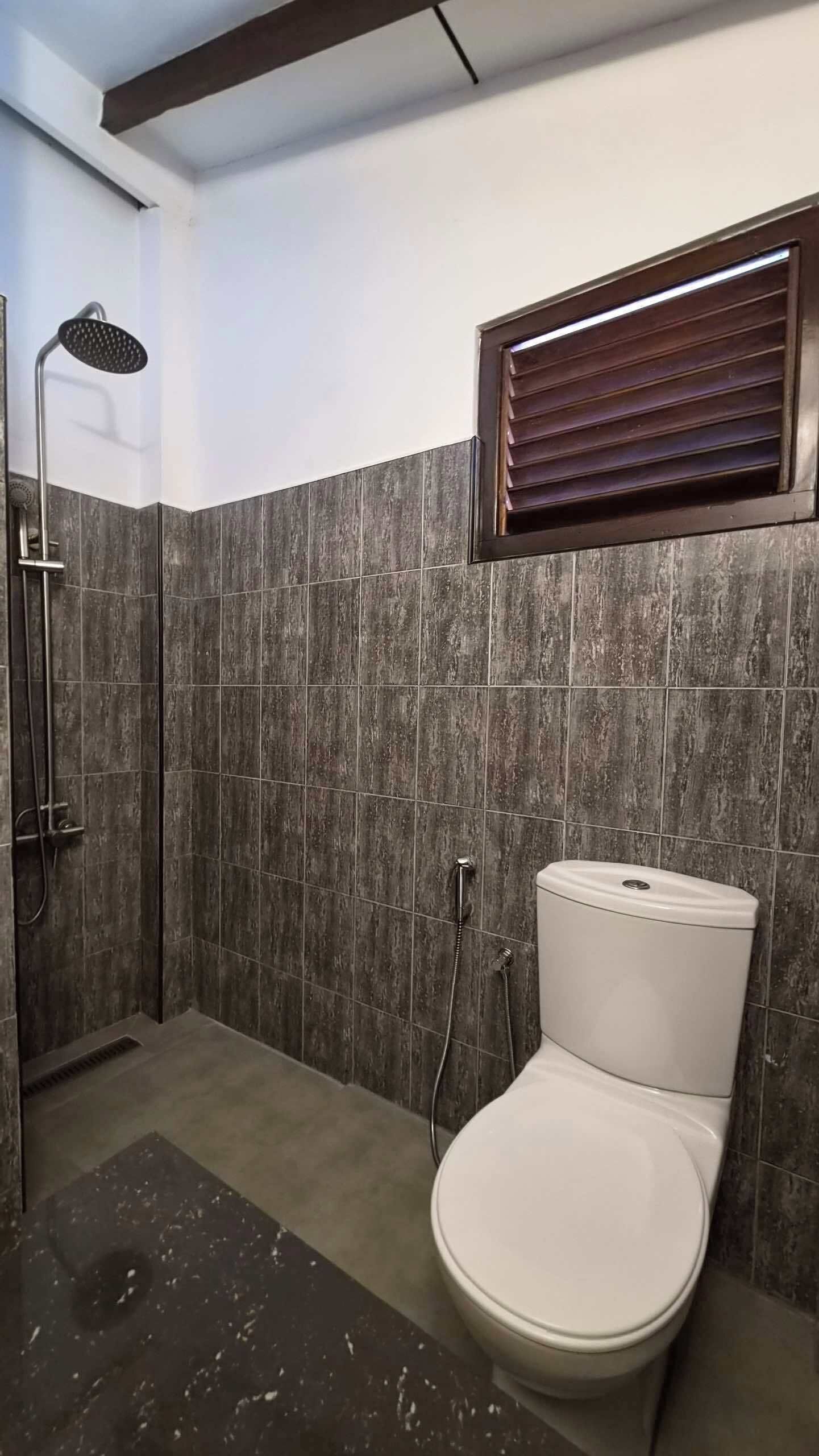 Un baño con ducha, inodoro y ventana con persianas.