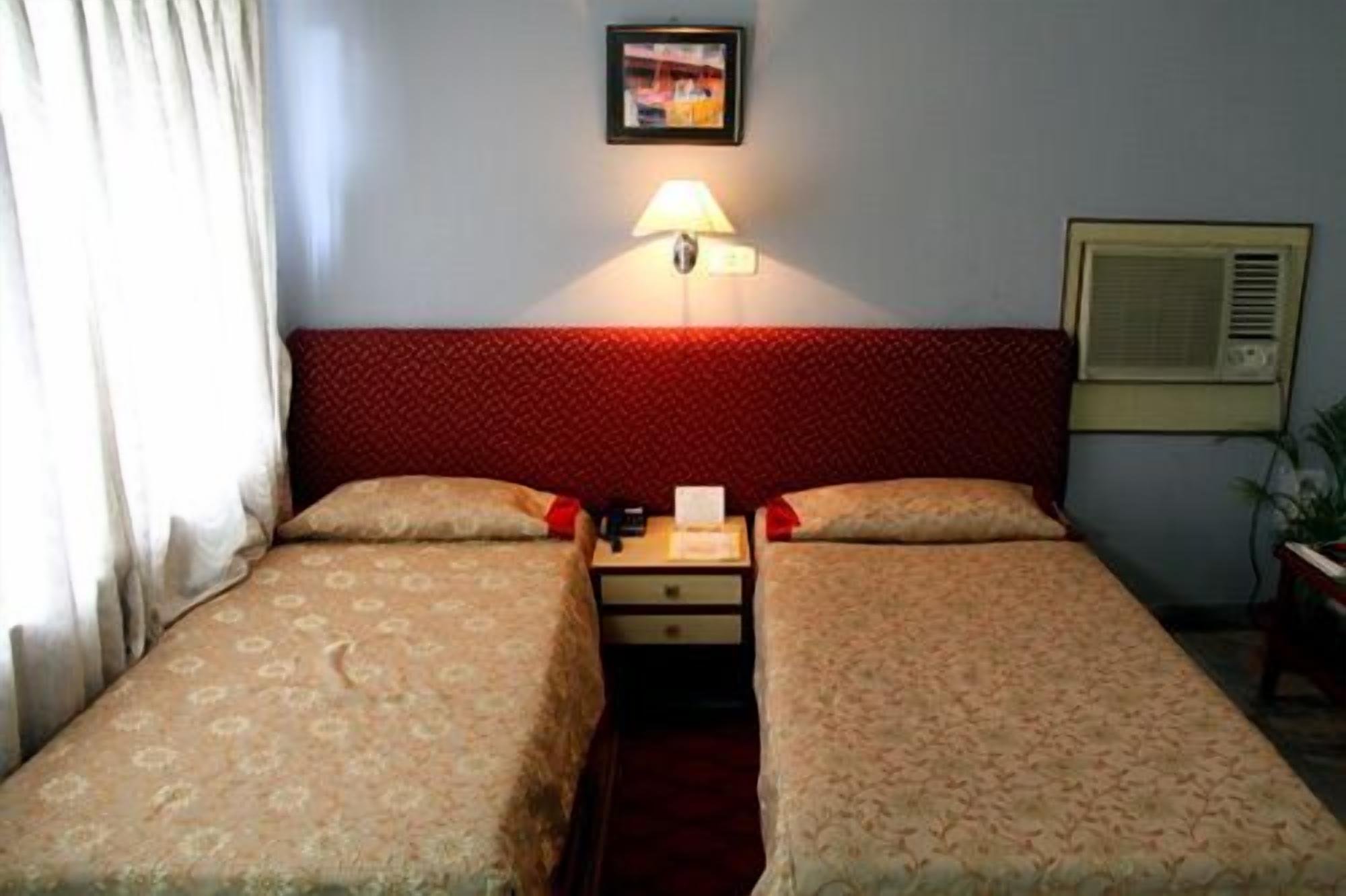 Hotelkamer met twee bedden, een nachtkastje, een lamp, een ingelijst foto aan de muur en een airconditioning.