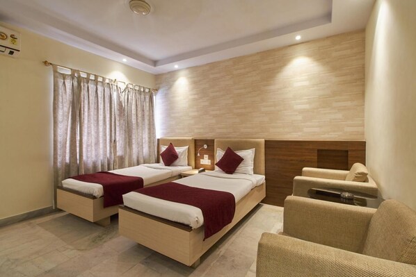 A hotel room with two beds, a sofa, and a small table. - Pallavi International Hotel (Kolkata)