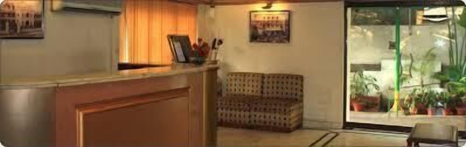 A reception area with a wooden desk, a patterned sofa, and a glass door leading to a balcony with potted plants.