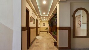 Un corridoio d'albergo con pavimento piastrellato, porte in legno, quadri appesi e piante in vaso.