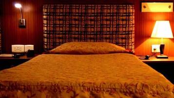 Habitación de hotel con una cama grande, cabecera estampada, mesita de noche con lámpara y un teléfono instalado en la pared.
