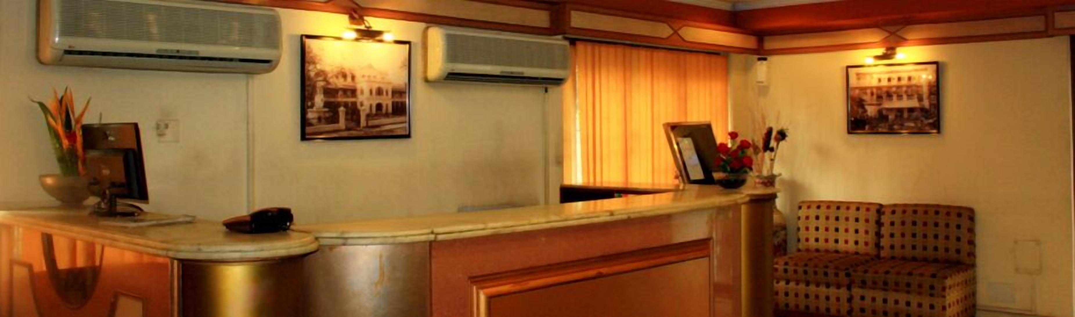 A room with a wooden counter, air conditioning units, a framed picture, a window with curtains, and a patterned sofa.
