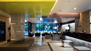 Un moderno vestíbulo de hotel con mostrador de recepción, zona de estar y grandes ventanales con vistas al exterior.