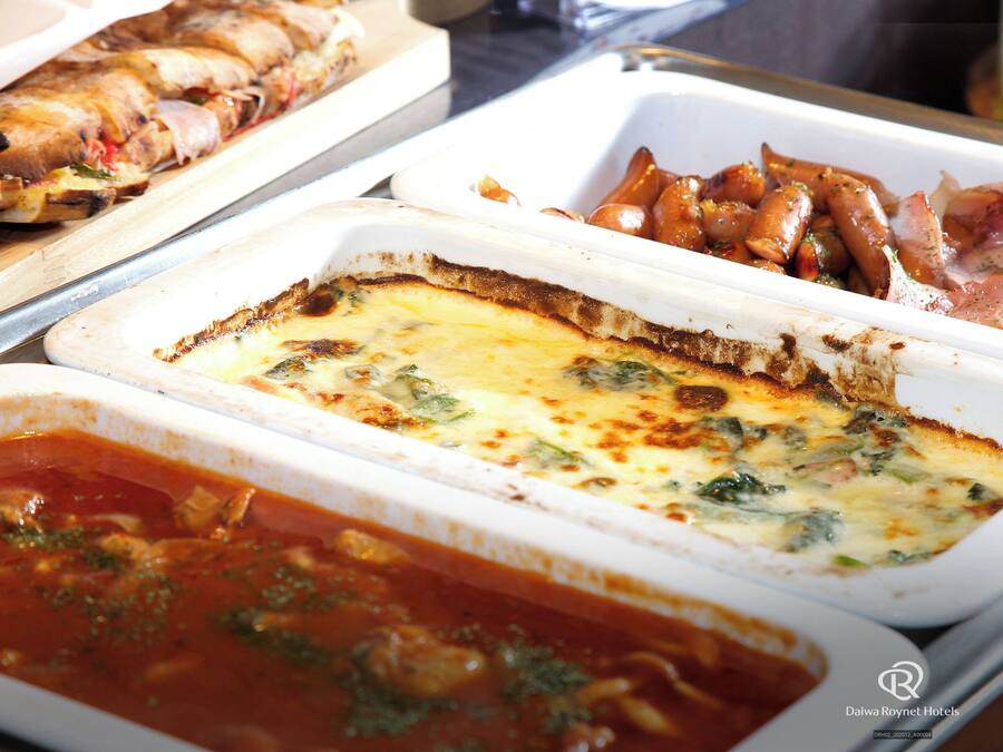 A buffet with various dishes including a quiche, roasted vegetables, and a pasta dish.