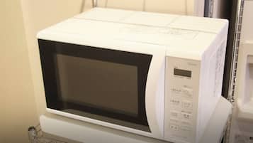 Un four à micro-ondes blanc, doté d’un écran numérique et d’un panneau de commande, est posé sur une étagère en métal dans une chambre d’hôtel.