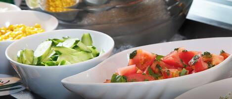 Un bufé con diversos platos, incluyendo una ensalada, rodajas de pepino y un plato a base de tomate.