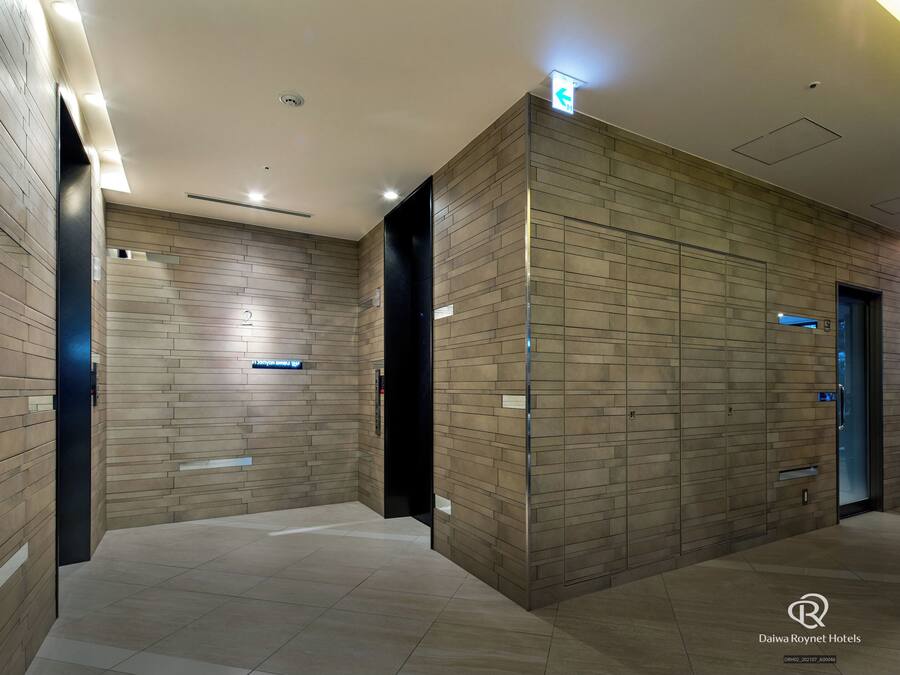 A modern hotel lobby with a tiled floor, a reception desk, and a wall-mounted elevator.