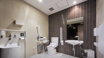 Une salle de bain moderne équipée de toilettes, d’un lavabo et d’une zone de douche, ainsi que de barres d’appui et d’un miroir.
