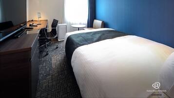 A hotel room with a bed, a desk with a computer, a chair, and a television.