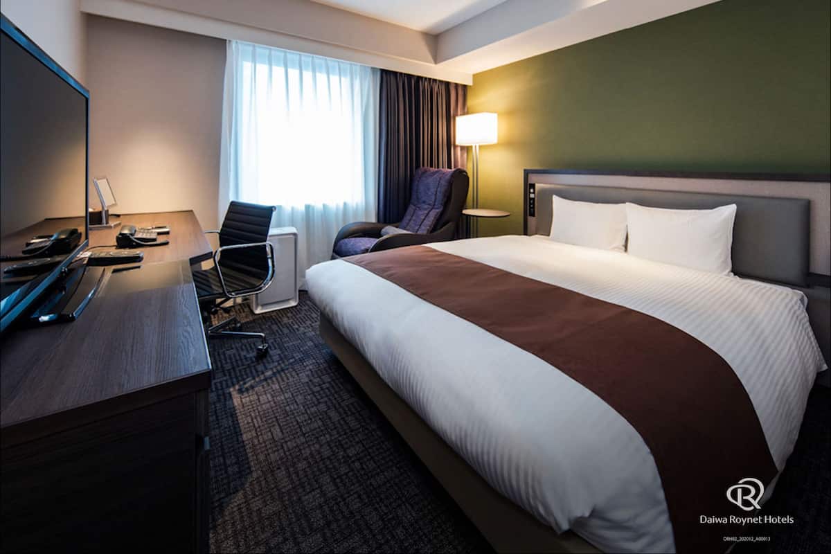 A hotel room with a bed, desk, chair, and a television.