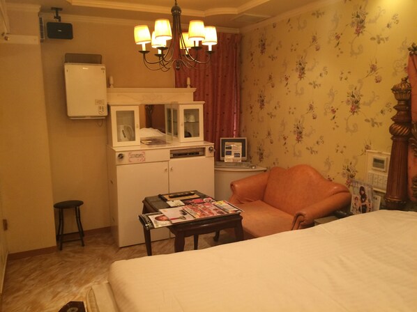 Habitación de hotel con cama, escritorio con revista, silla, televisor y minibar.