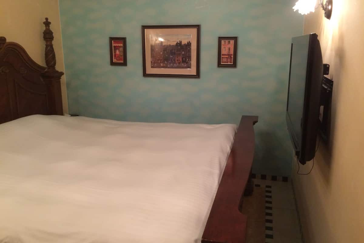 Une chambre avec un lit, un téléviseur fixé au mur et des tableaux encadrés.