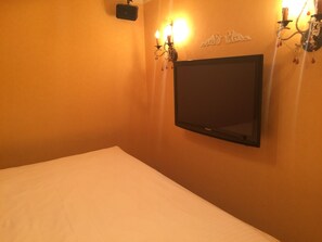 Habitación de hotel con cama, televisor de pantalla plana en la pared y dos apliques con velas.