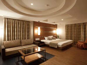 Ein modernes Hotelzimmer mit einem großen Bett, einer Couch, einem Glastisch und Holzboden.