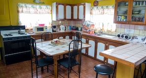 A kitchen with a stove, microwave, and cabinets. There is a dining table with chairs and a window with curtains.