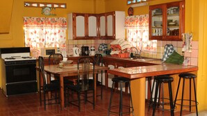 A kitchen with a stove, microwave, and various appliances. There are chairs and stools around a central island. - Villa Shalom Guest House (Port of Spain)