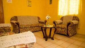 A room with two floral-patterned sofas, a small round table with a vase, and a bed with a white blanket. - Villa Shalom Guest House (Port of Spain)