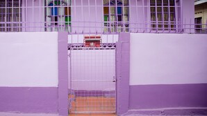 A purple-walled building with a metal gate and a small window. - Villa Shalom Guest House (Port of Spain)