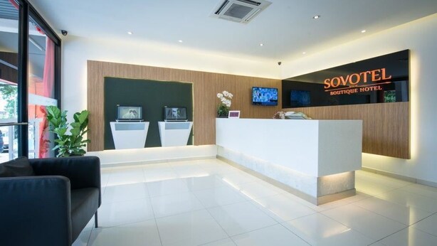 Een moderne hotel receptie met een strak, minimalistisch design, met een receptiebalie, twee zithoeken en een groot scherm dat inhoud toont.
