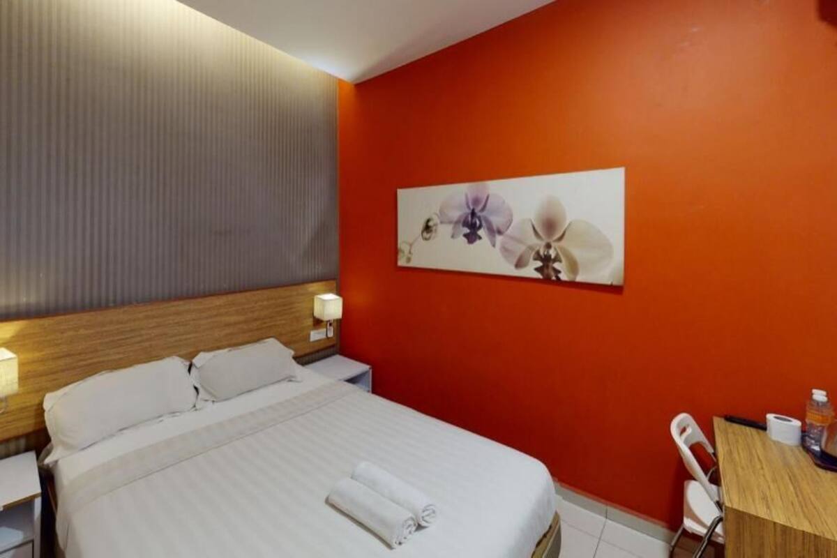 Een hotelkamer met een bed, nachtkastje, bureau en stoel.