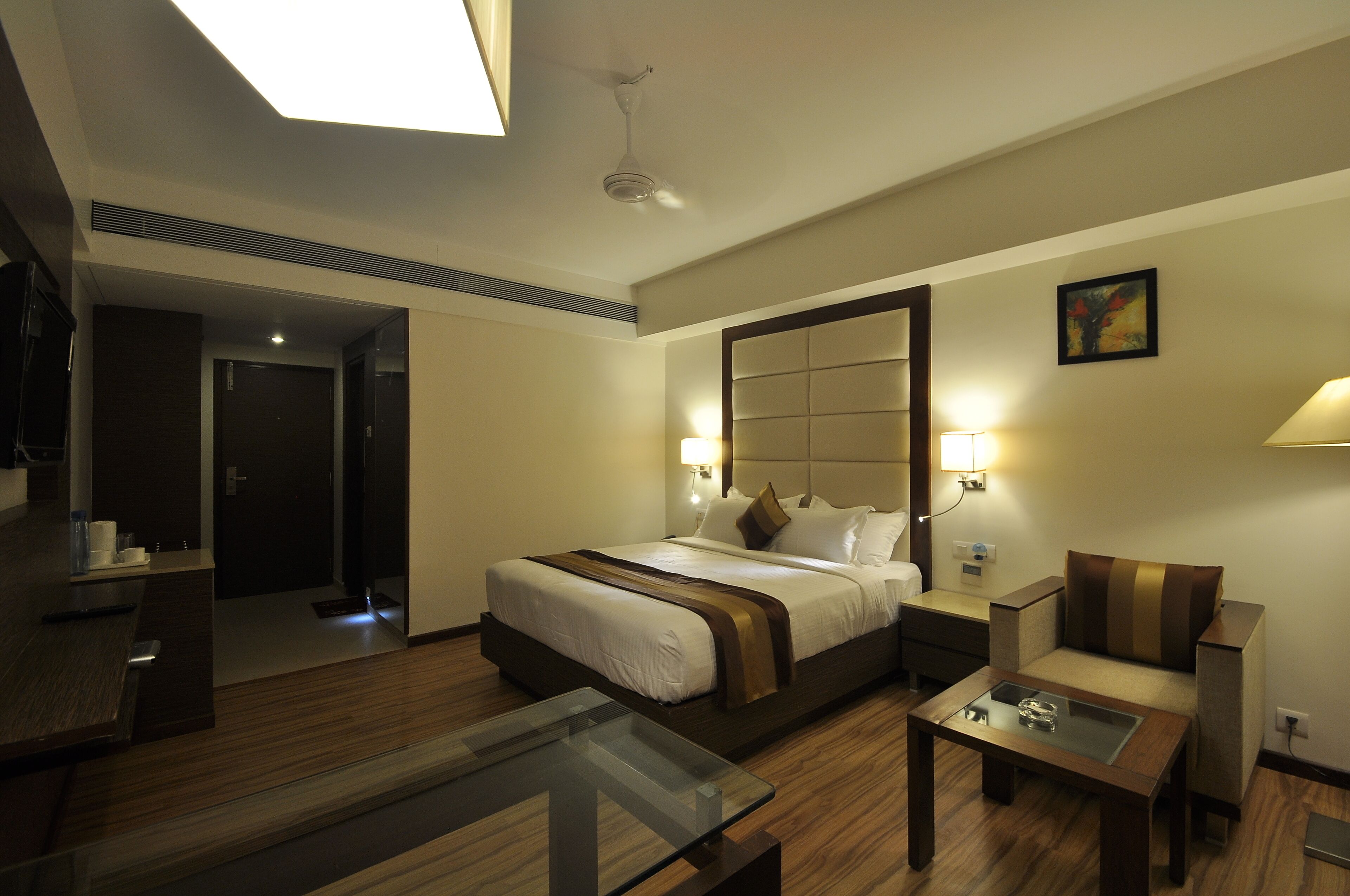 Habitación de hotel con una cama grande, lámparas de noche, un sofá, una mesa de centro de vidrio y un espejo.
