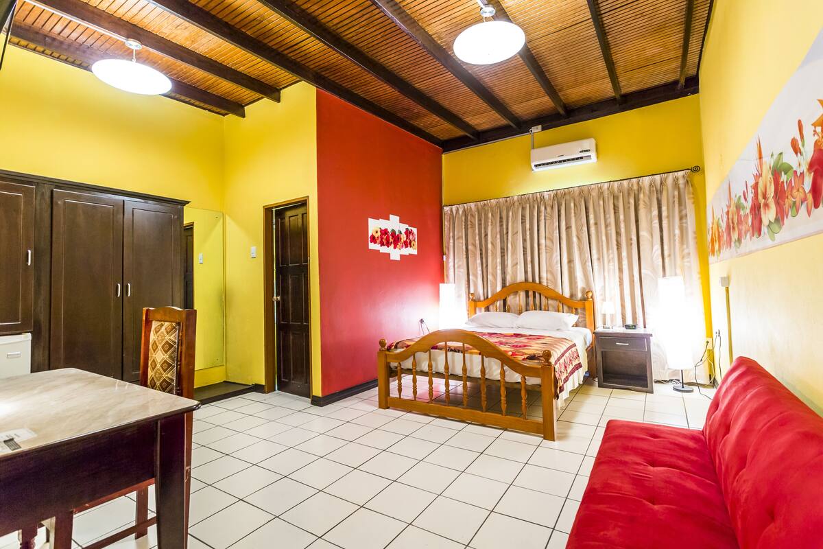 Una habitación con una cama, un sofá rojo, una mesa de madera y un armario.
