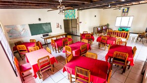 A classroom with wooden tables and chairs, red tablecloths, a blackboard, a map, and a television. - Par May La's Inn (Port of Spain)