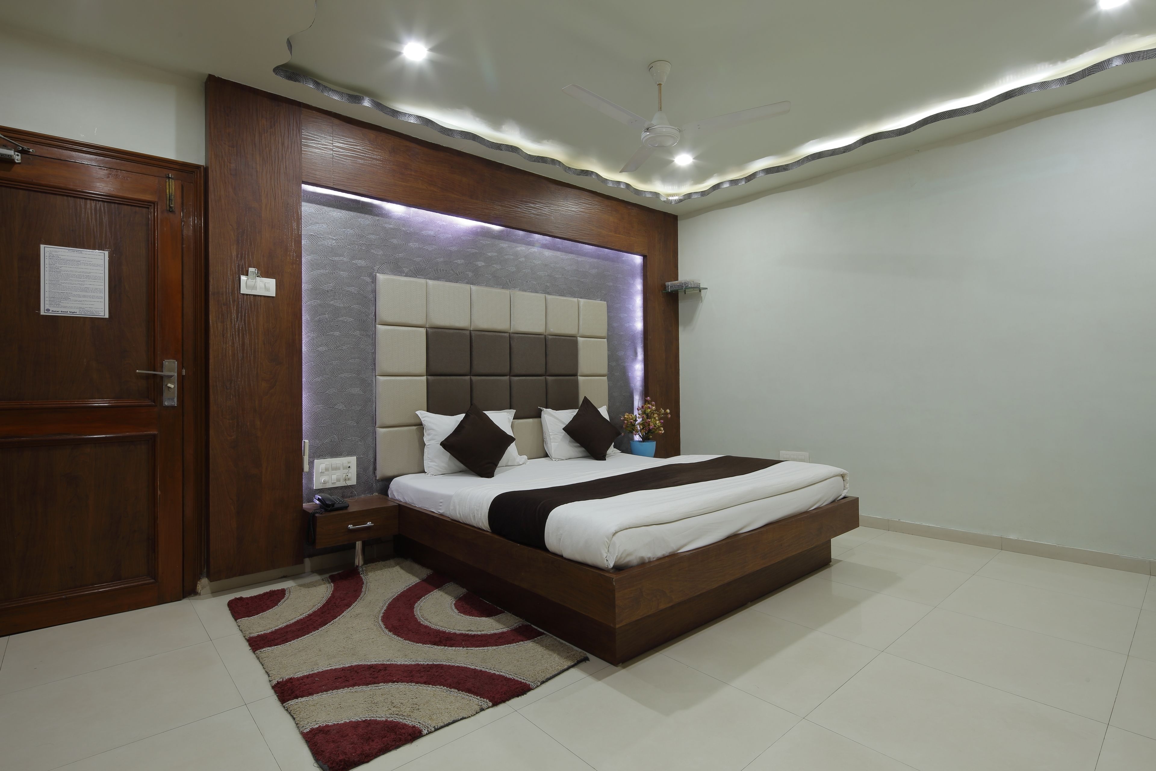 A bedroom with a wooden bed frame, a headboard with a built-in light, a nightstand, and a red and white rug.