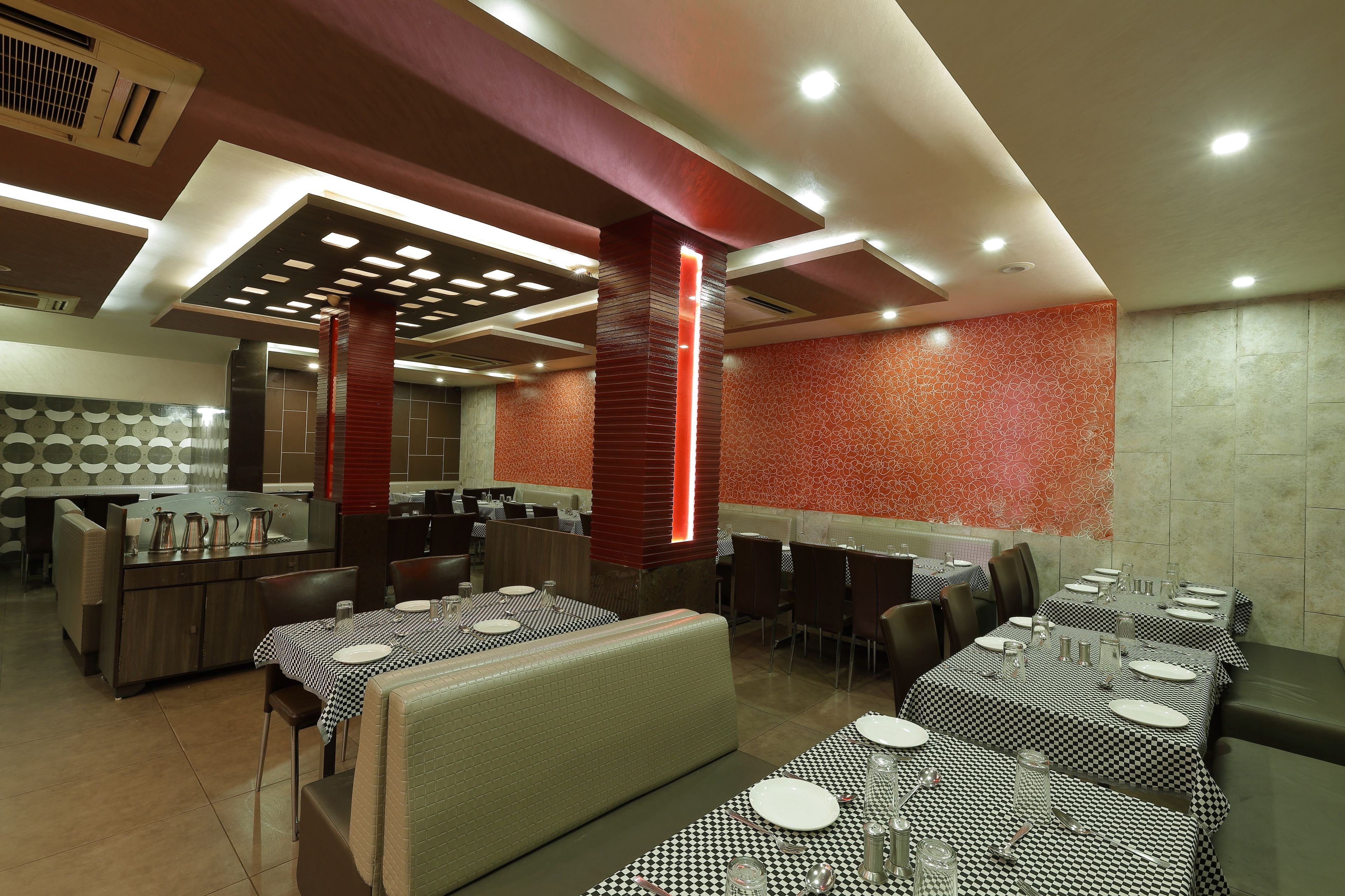 Un restaurante con varias áreas de comedor, incluyendo boxes y mesas, con un diseño de techo moderno y detalles en rojo.
