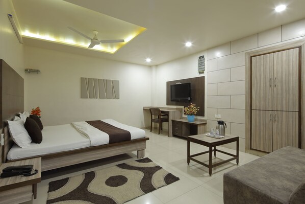A modern hotel room with a bed, desk, TV, wardrobe, and a ceiling fan.