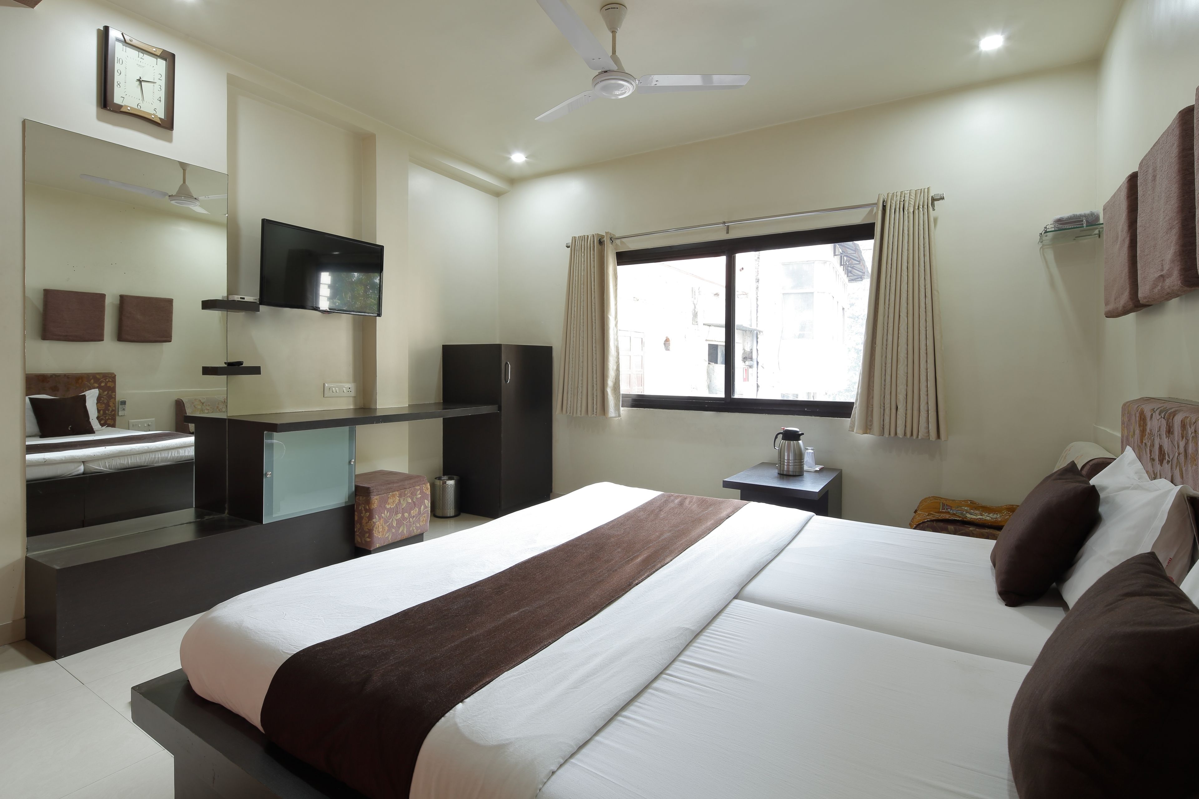 A hotel room with a bed, a desk, a television, a window with curtains, and a ceiling fan.