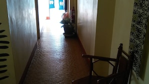 Un couloir avec un sol carrelé, une chaise en bois et une porte au fond.