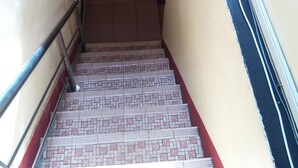 Un escalier étroit avec des carreaux décorés, une rampe métallique et un mur à rayures.