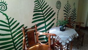 Un coin repas avec une table et des chaises, une plante en pot et des décorations murales évoquant des fougères.