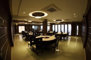 A modern dining area with round tables and chairs, recessed ceiling lighting, and a polished floor. -  Pearl Hotel & Banquets (Sanand)