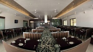 Een modern restaurant met een lange centrale tafel, omringd door zithoeken, voorzien van plafondventilatoren en inbouwverlichting.