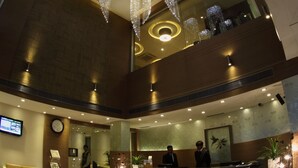 Een hotel lobby met een receptiebalie, een grote kroonluchter en een klok aan de muur.