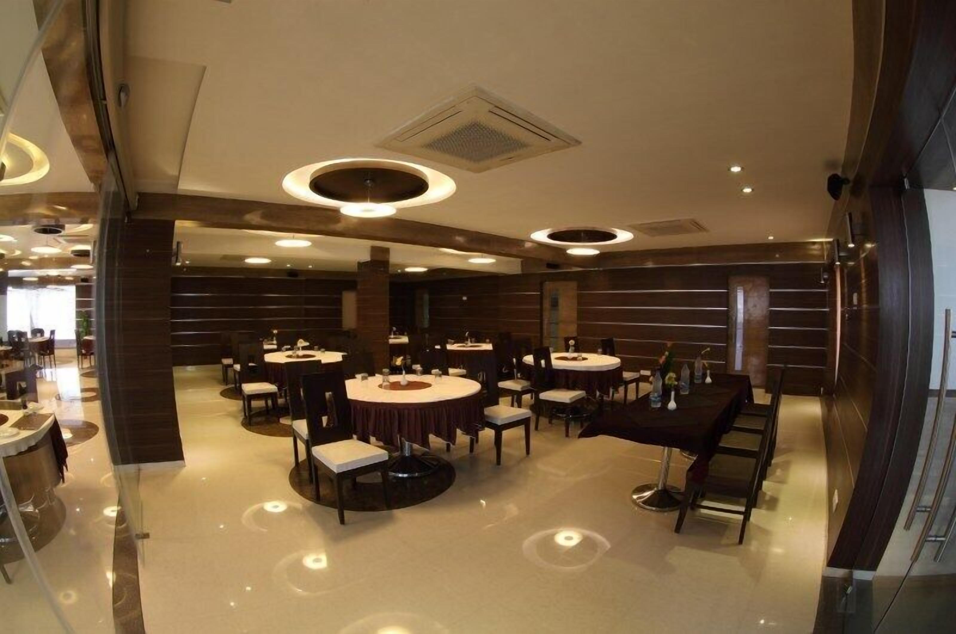 A modern dining area with round tables and chairs, recessed ceiling lights, and a polished floor.