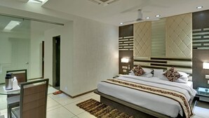 Een moderne hotelkamer met een groot bed, een glazen scheidingswand, een bureau met stoel en een grote spiegel.