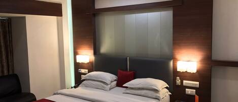 A modern hotel room with a large bed, two bedside tables, a desk, and a chair.