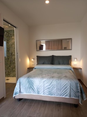 A bedroom with a bed, a glass shower, and a mirror on the wall.