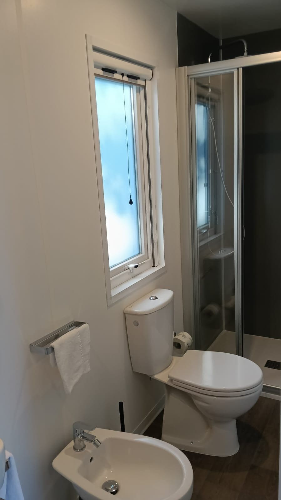 Et badeværelse med toilet, vask og en brusekabine med glasvægge.