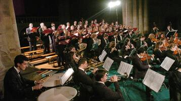 A large orchestra performing on stage with musicians seated and standing, and music stands visible.